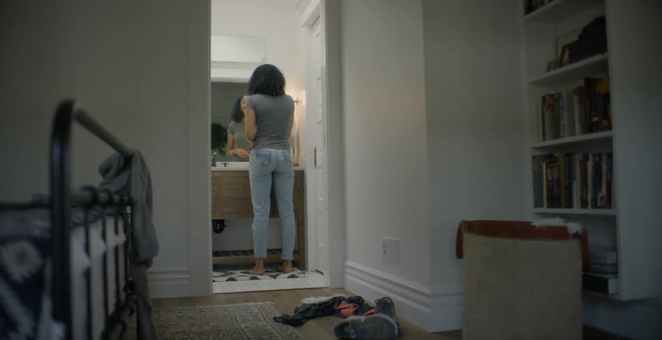 The woman is standing in the bathroom as the dog turns the corner