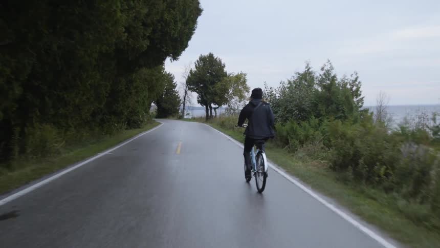 Woman is riding bike on wet coastal road overlooking ocean