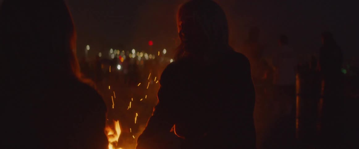 Two women talk next to a bonfire at night