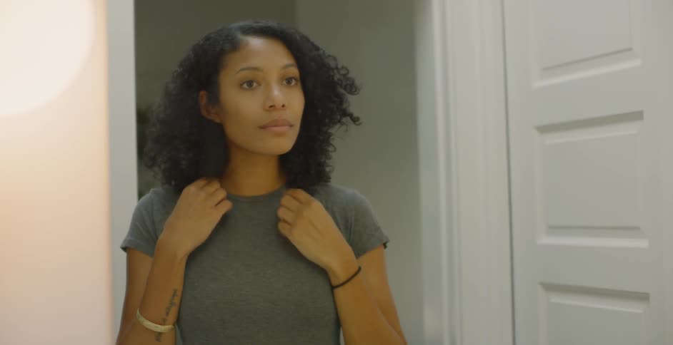 The woman is brushing and adjusting her hair in the bathroom