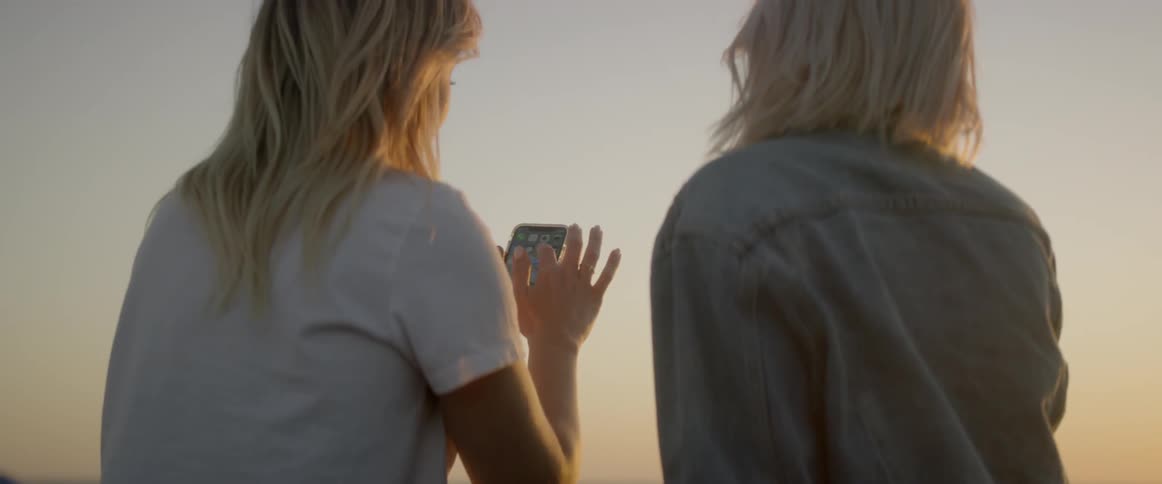 The two women use a phone on the beach