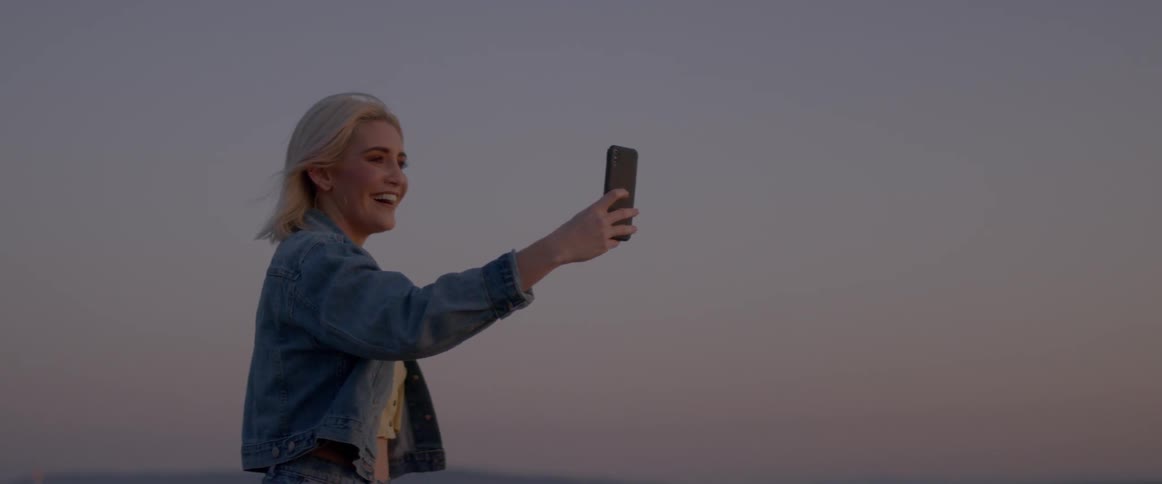 Woman with blond hair laughs as she looks at her cellphone