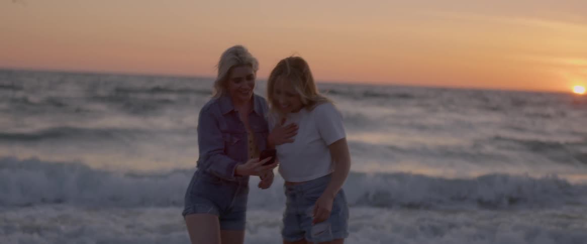 Woman runs on the beach and shows her phone to another woman
