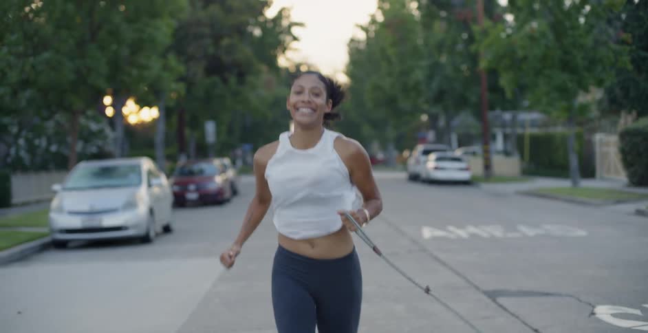 Woman jogs down the street as a dog runs next to her on its leash