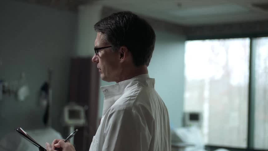A doctor writing on a chart and nodding while in a hospital room