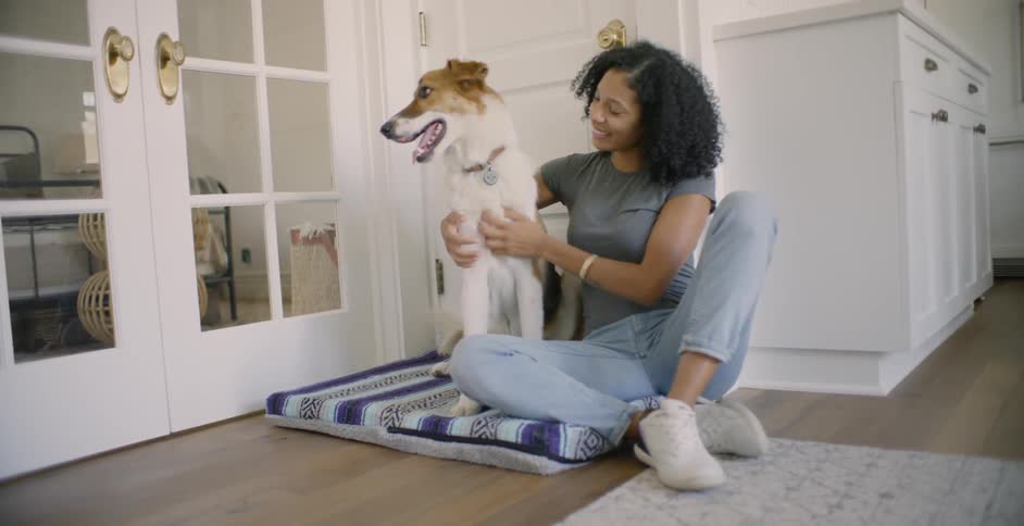 A woman sits next to her dog on his dog bed and pets him
