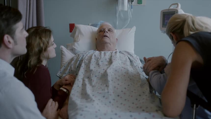 Elderly man in a hospital bed with several people surrounding him