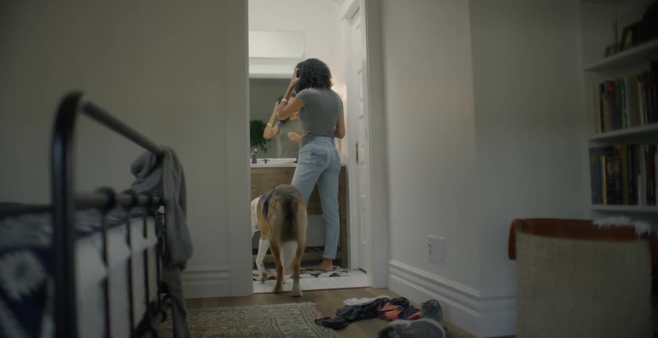 A dog watches a woman style her hair in a bathroom