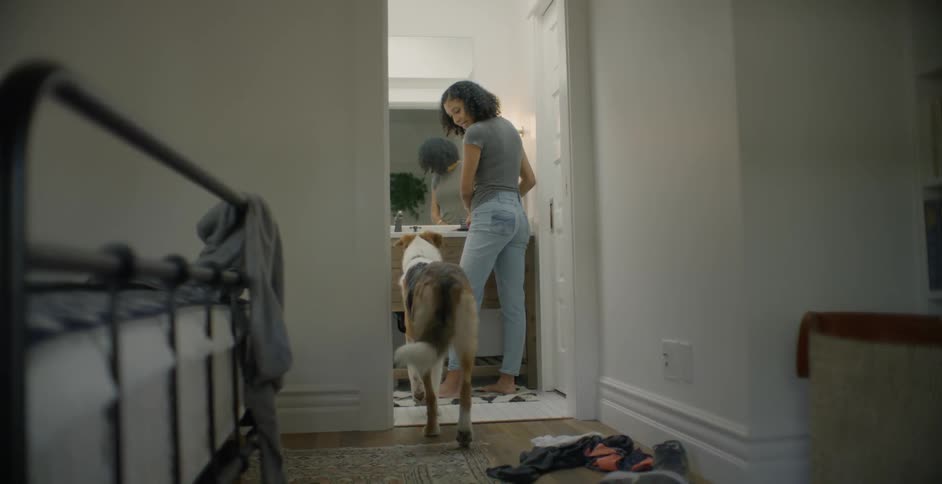 A dog enters the bathroom where a woman is standing and he sits on command