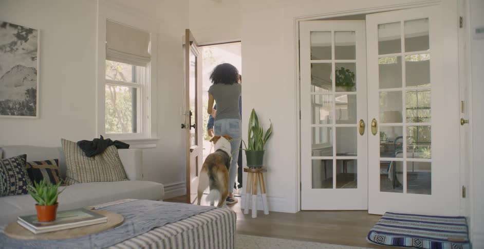 The woman opens the door and tries to keep the dog inside