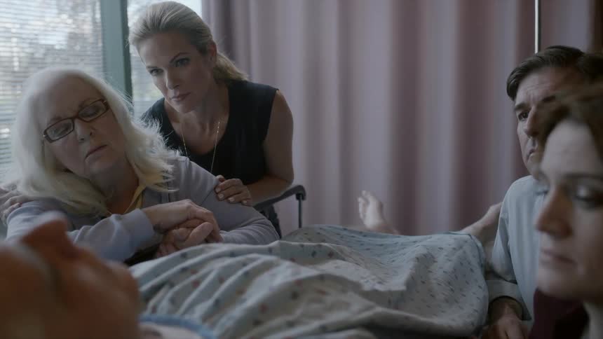 A family gathered around the hospital bed of an elderly man who appears very ill