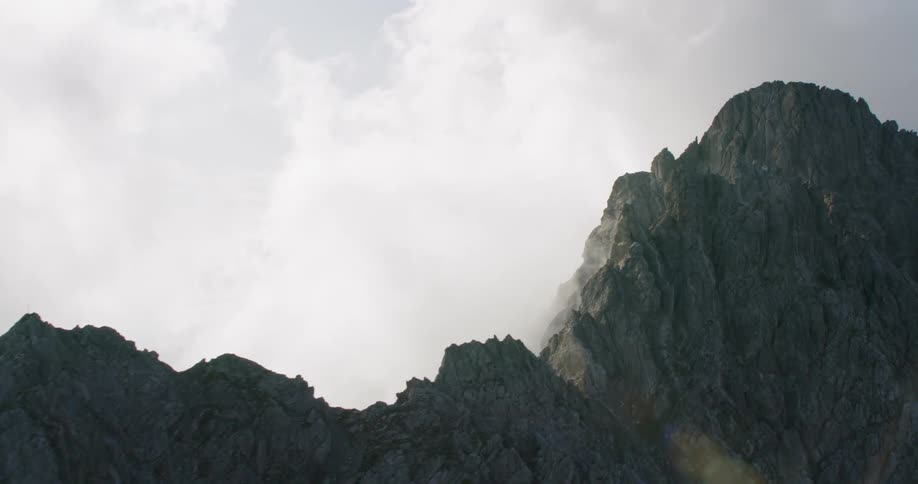 The tall mountains have clouds moving over the top