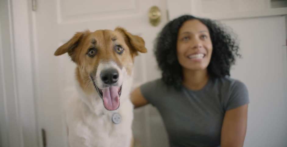 A woman sits on the floor and pets her dog as she talks and smiles