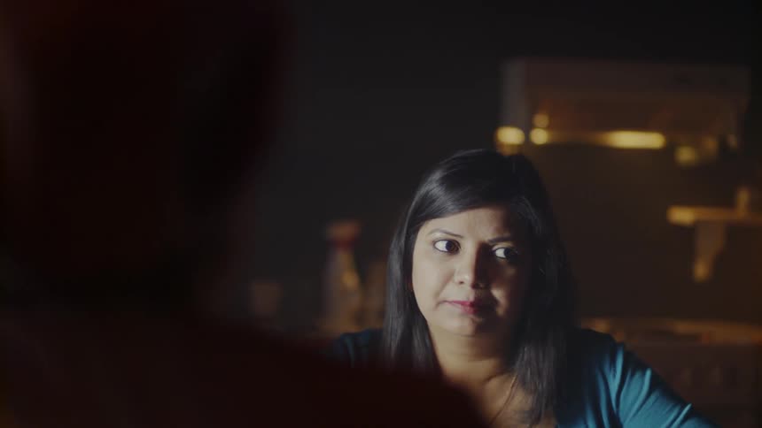 The woman talks with others in the dark dining room