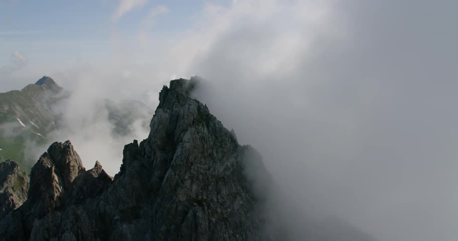 Clouds billow over tall rocky mountains