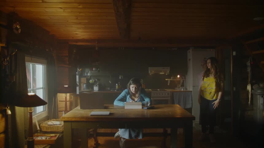 Woman works at a table while two women pace behind her
