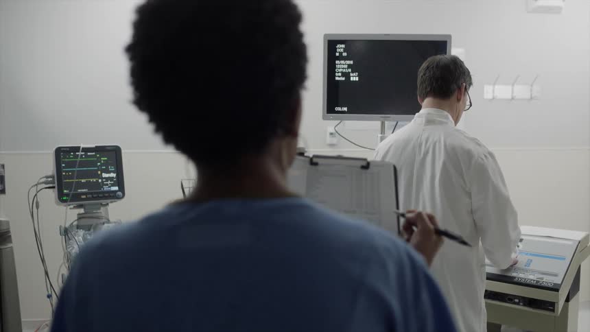 Nurse writing on a chart while a doctor observes his monitor