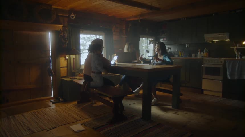 A child is climbing up on a table bench inside a house where two adults are talking