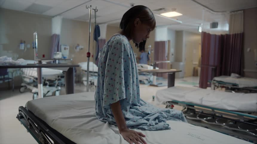 A woman in a hospital gown is sitting on the edge of the bed