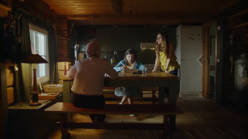 A woman inside a house is talking to two other women who are seated at a table