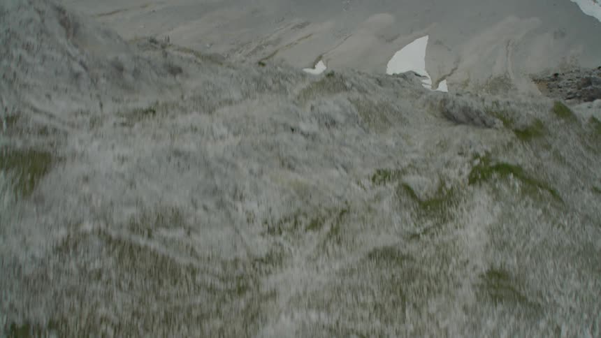 Tall mountains dotted with snow loom over a valley on a cloudy day