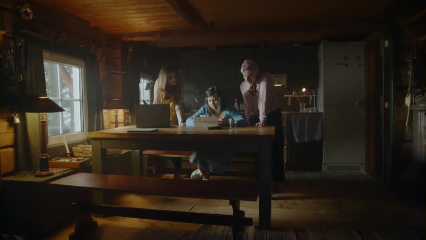 Women are gathered around a tablet in a dark dining room