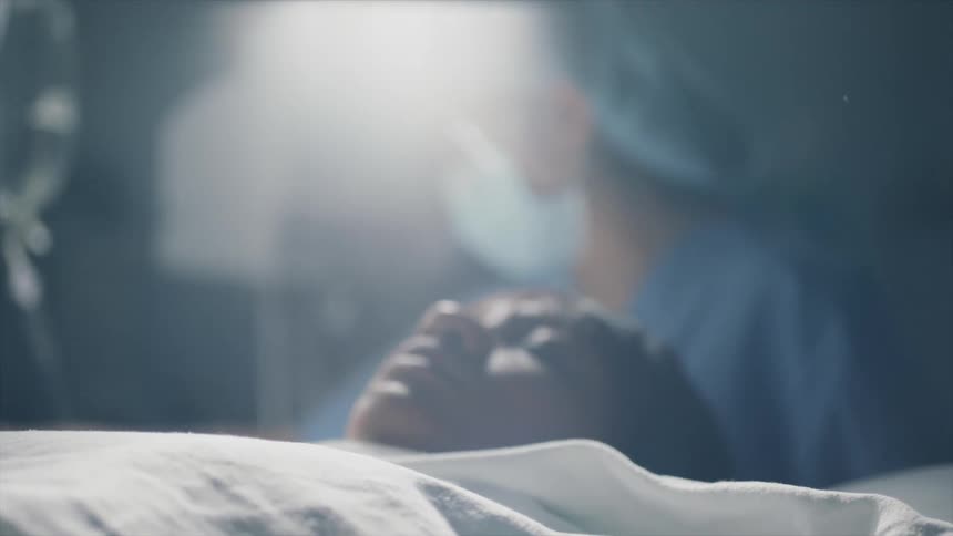A woman lying on a bed as a doctor checks an iv bag