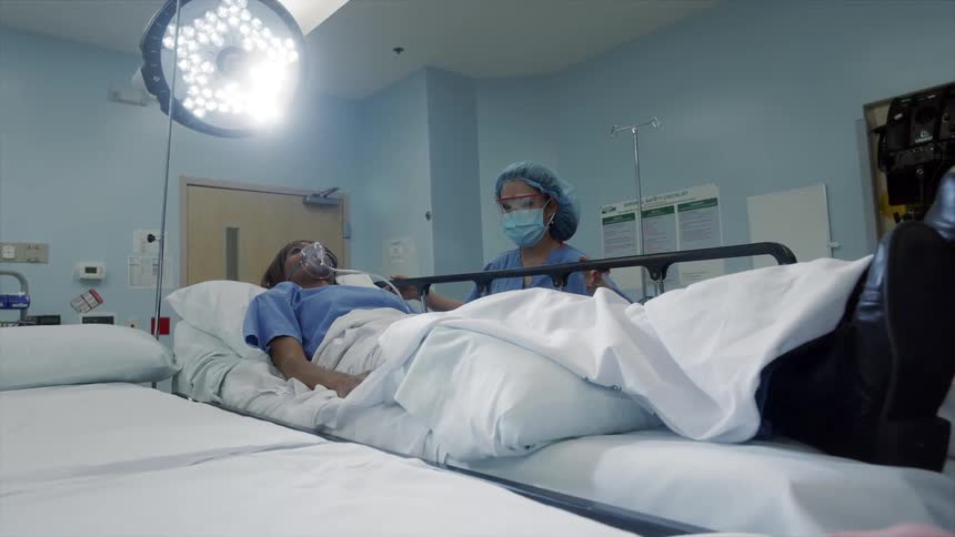 A woman lays on a hospital bed while being spoken to by a female nurse