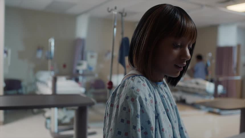 A woman in a hospital gown sitting on a bed is looking down