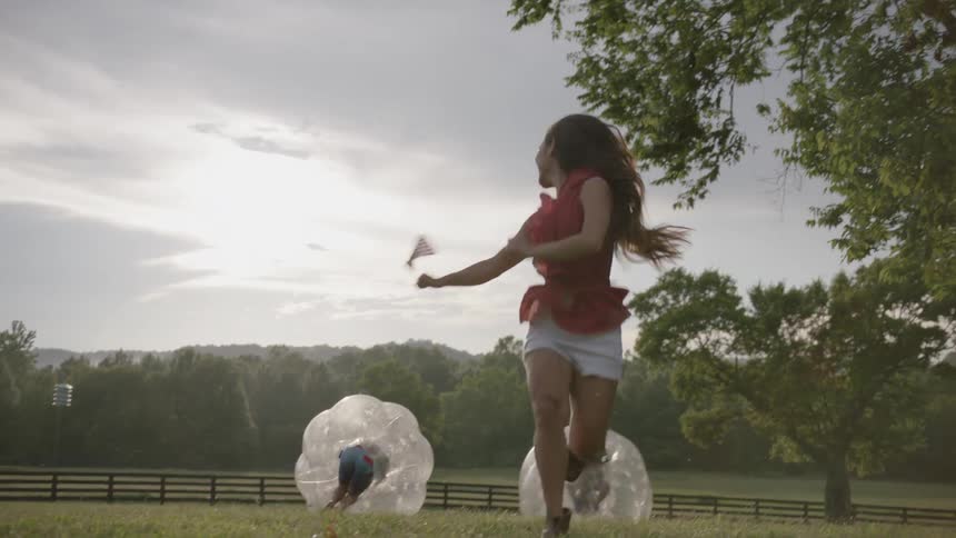 The woman waves off a race between two people in inflated bubbles