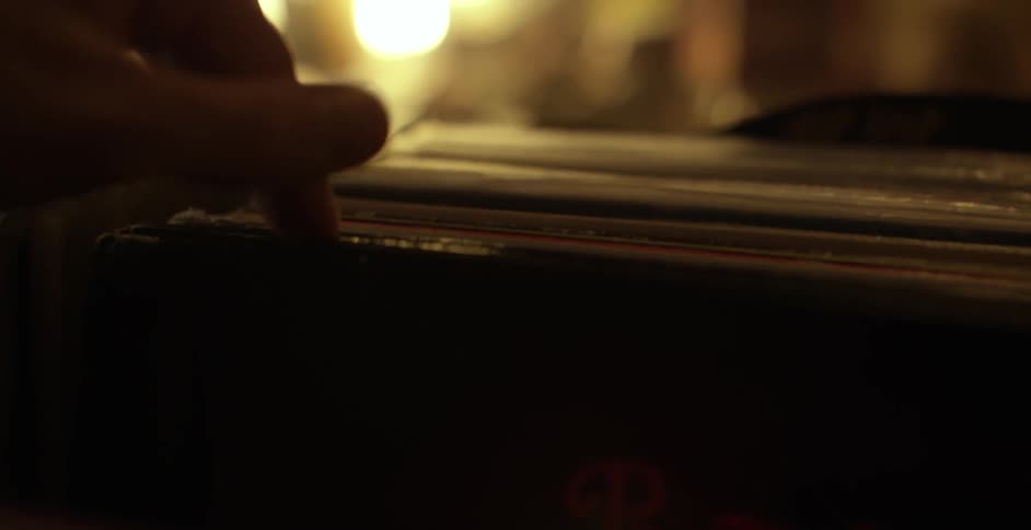 A hand flips through record albums in a dimly lit shop