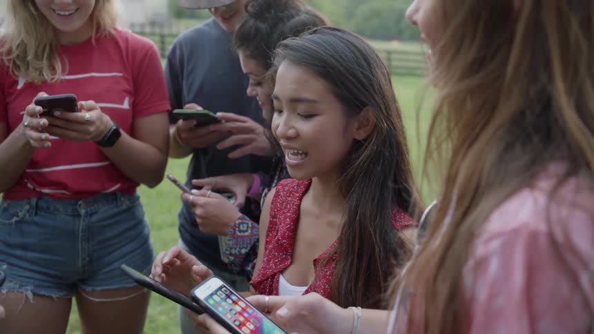 A group of people smile while using their cell phones outside on a grassy lawn