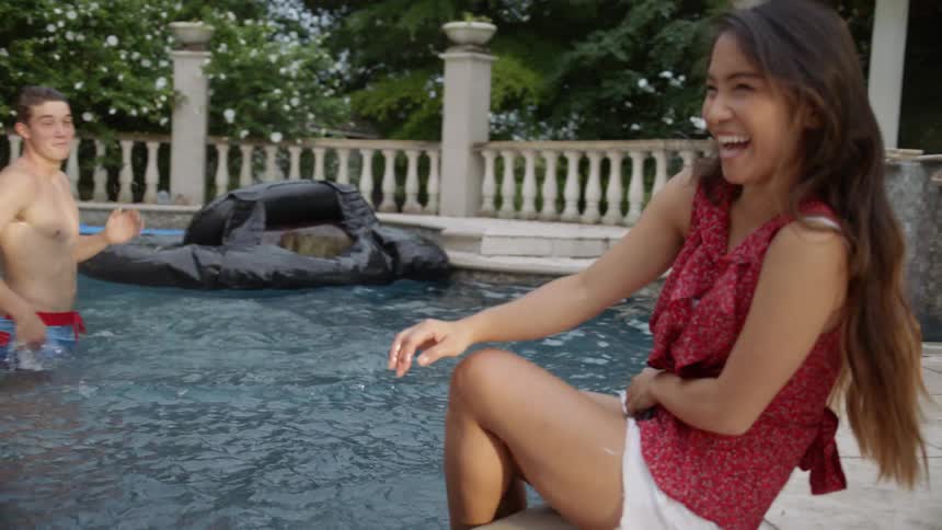 Man and woman splash water at each other in a pool