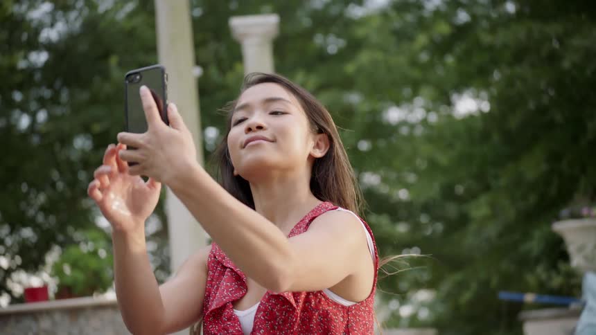 A woman is smiling as she takes a selfie outside in daylight