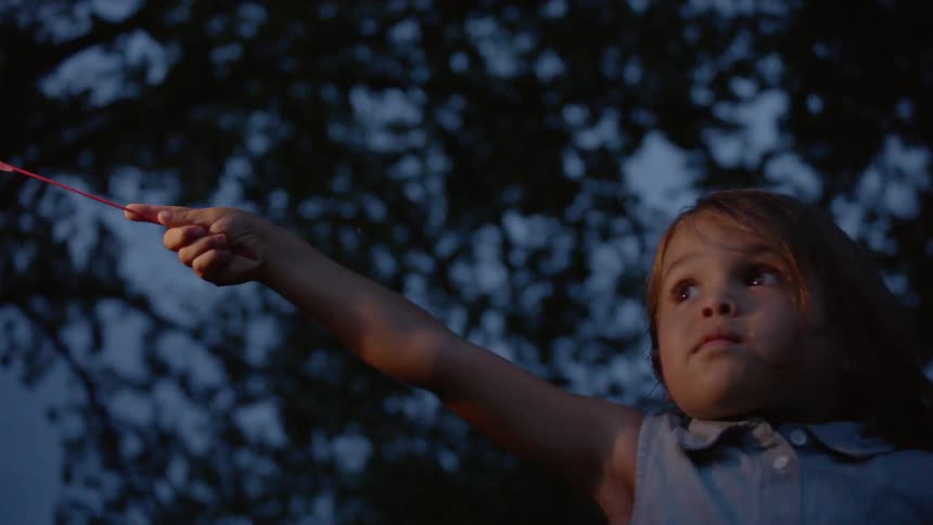 The child holds up her sparkler at sunset