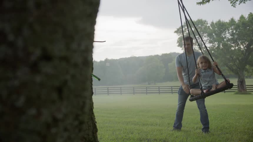 Father is pushing daughter on tree swing on cloudy day