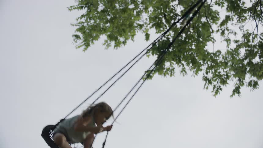 Child rides on a small circular swing by a tree