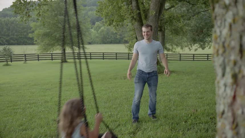 Father is pushing daughter on tree swing in field