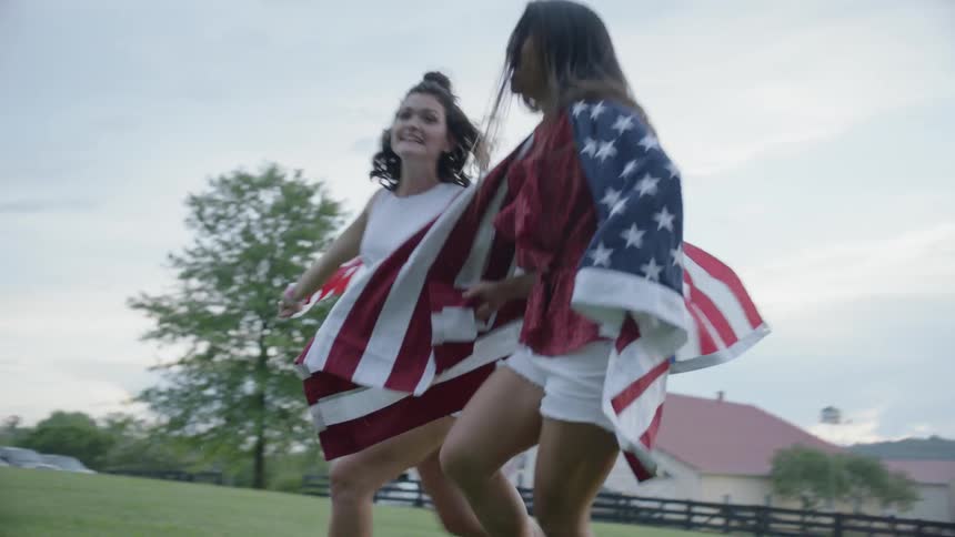Two girls are running in grass with american flags on farm