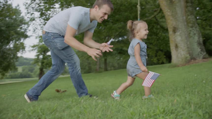 The child is swing in the arms of the man while she holds a flag
