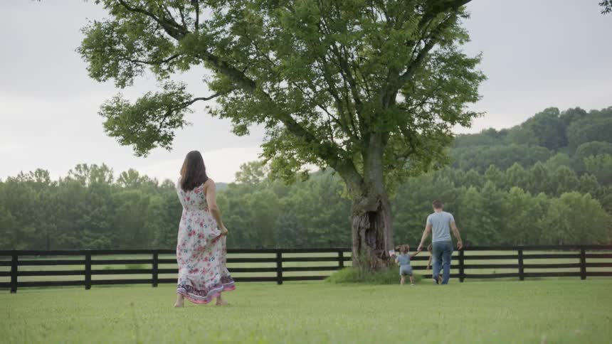 A mom carrying a baby follows her husband and children through the grassy field
