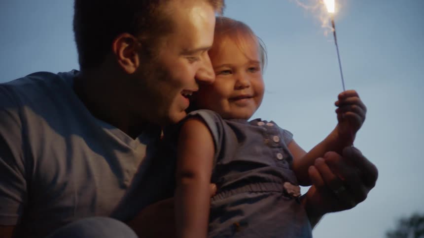 The child holds the sparkler as the man holds her