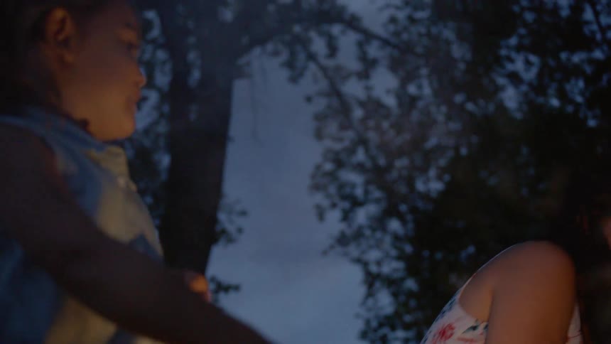 A mom laughs as she watches her daughter wave around a sparkler in the yard