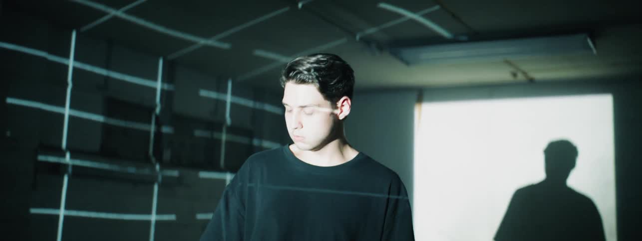 A man walks and turns in a dark room with a grid of light on the wall
