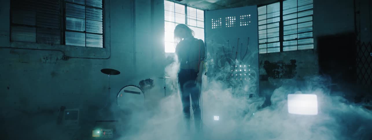 Woman poses in front of a drum set with smoke billowing around her