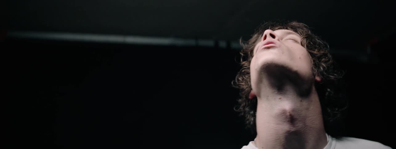 Man stands in a dark room lit by one light looks up and closes his eyes
