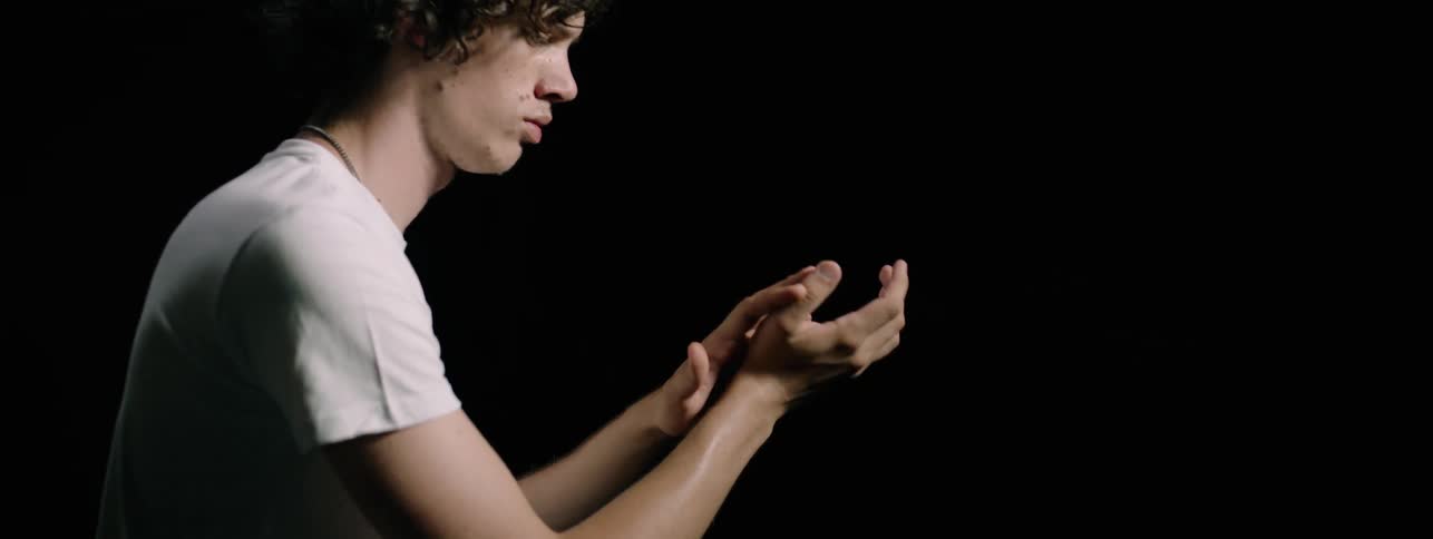 Man stands in a dark room looking at his hands