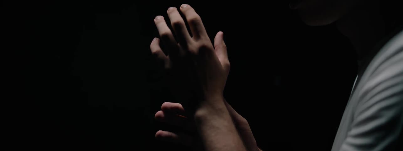 The man examines his hands in the dark