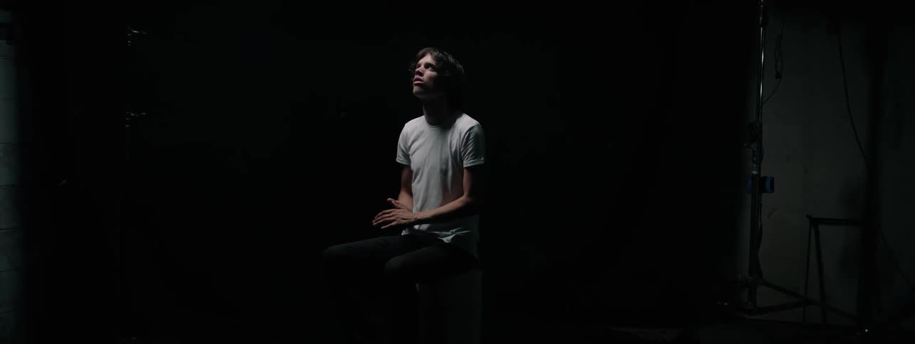 The man folds his hands together sitting in the dark room