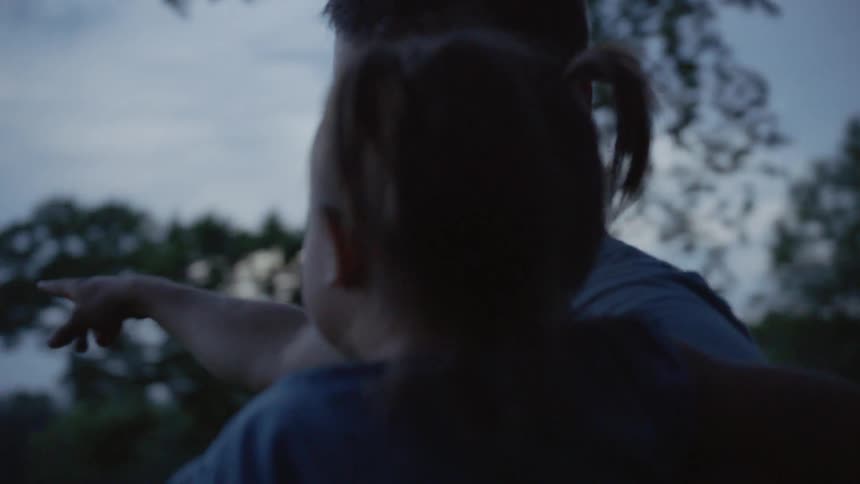 Father holds young girl and points to fireworks